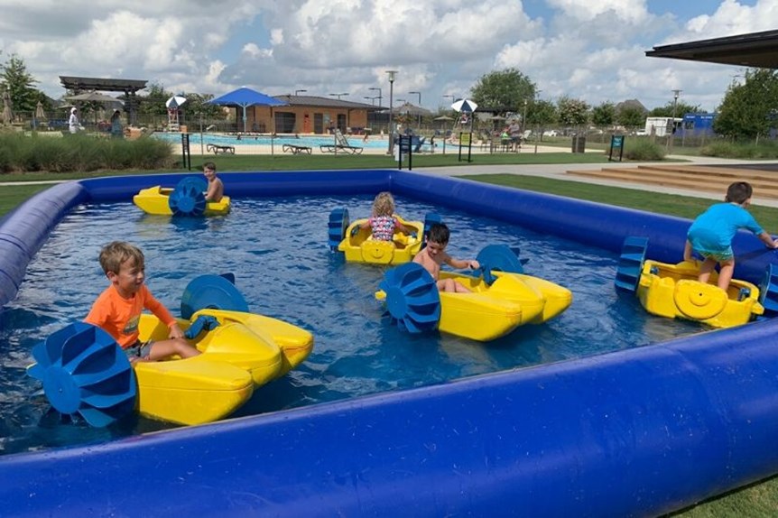 Children riding paddle boats in an inflatable pool during a summer event at Elyson in Katy, TX.