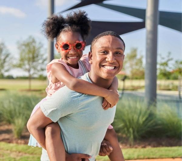 Brother giving little sister a piggyback ride at Elyson Commons