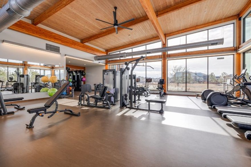 Elyson fitness center at Elyson House in Katy, TX, with cardio machines, strength equipment, wood-beamed ceilings, and floor-to-ceiling windows.