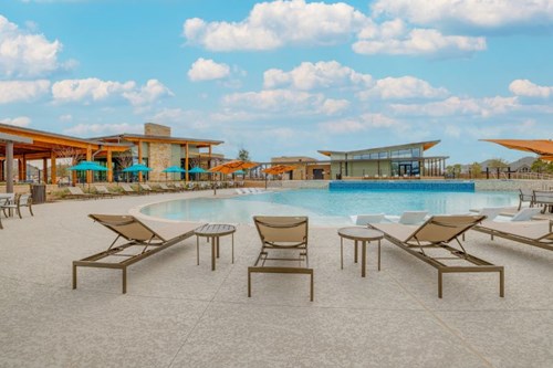 : Resort-style pool and amenity center for residents of new homes at Elyson, with lounge chairs, shade umbrellas, and fitness building