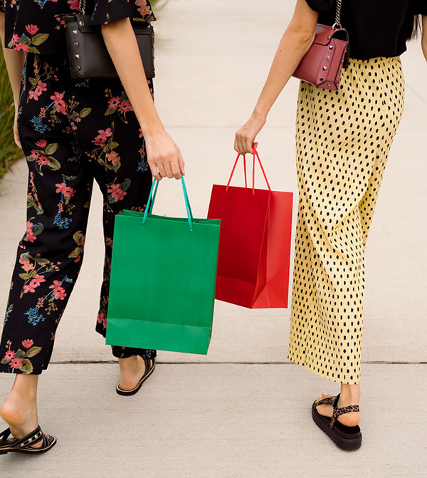 two people walking on sidewalk with shopping bags